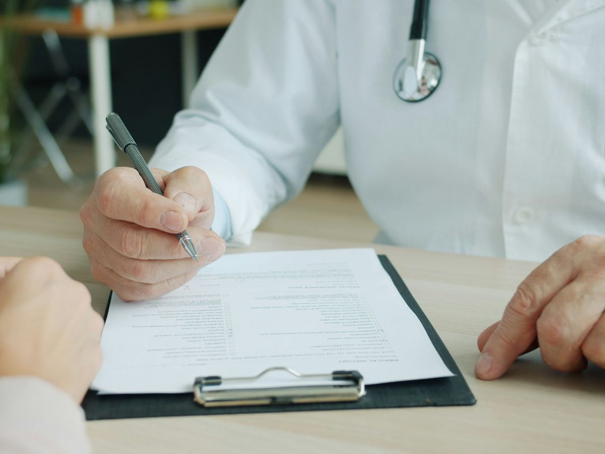 Médico anotando la historia clínica durante la valoración de la caída del pelo